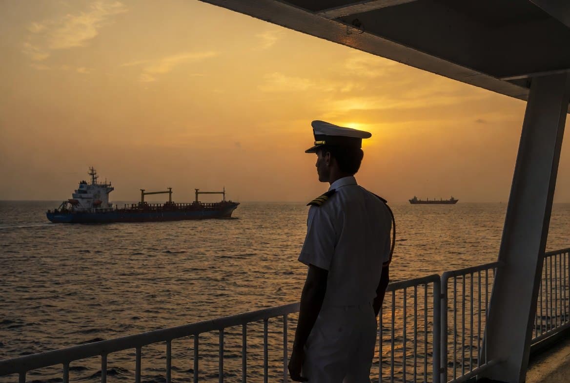 A Merchant Navy officer on deck watching a vessel at sunset